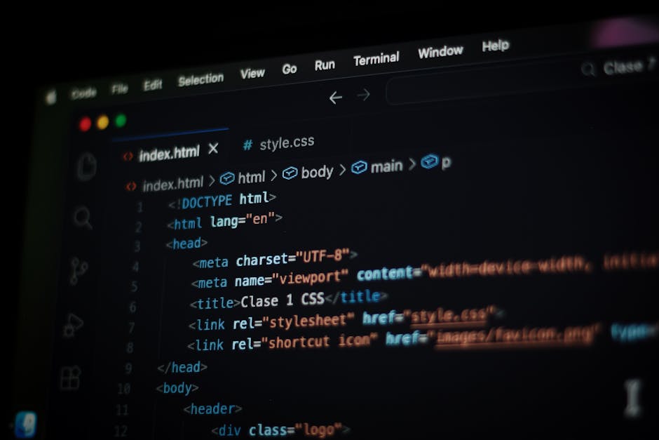 A close-up of a laptop screen displaying lines of colorful programming code with syntax highlighting, set in a bright workspace with blurred background elements such as another laptop and a person wor